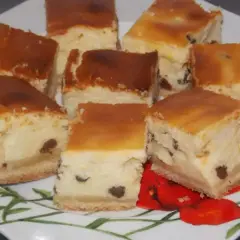 Sernik, który każdemu wychodzi, pokrojony w kostkę, z rodzynkami, na talerzu z czerwonymi makami.