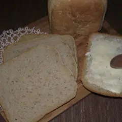Chleb pszenno żytni na zakwasie, pokrojony w kromki. Jedna kromka posmarowana masłem, obok leżą kolejne.