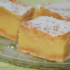 Kawałki puszystego ciasta napoleon z kremem budyniowym, posypane cukrem pudrem, na szklanej paterze.