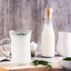 Szklanka z napojem, butelka i dzbanek mleka, gałązka koperku. Poznaj kefir właściwości dla zdrowia.