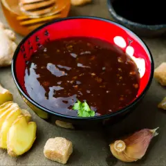 Sos teriyaki przepis: miseczka z ciemnym sosem, obok imbir, czosnek, cukier i miód. Idealny do dań azjatyckich.