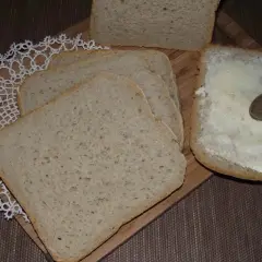 Chleb pszenno-żytni pokrojony w kromki, jedna z nich smarowana masłem. Idealny przepis na domowy wypiek.