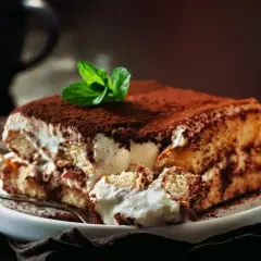Pyszny, sprawdzony przepis na tiramisu z mascarpone. Kremowe warstwy biszkoptów i mascarpone, posypane kakao, z listkiem mięty.