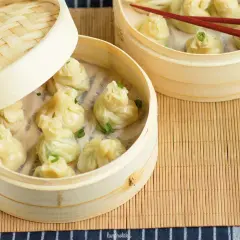 Parujące pierożki z ciasta do wontonów w bambusowych parownikach, ozdobione szczypiorkiem.
