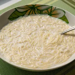 Zupa mleczna z makaronem, podana w misce z motywem kwiatowym. Widoczna łyżeczka zanurzona w kremowym daniu.