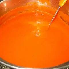 Gęsty, pomarańczowy sos do gołąbków w metalowym garnku, z widoczną igłą termometru.