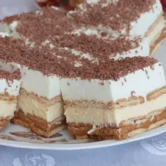Szybkie ciasto bez pieczenia z budyniem i herbatnikami, przełożone kremem i posypane wiórkami czekoladowymi.