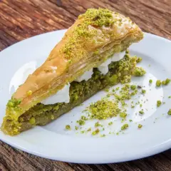 Pyszne ciasto na baklawę, warstwowe, z kremem i posypane pistacjami, na białym talerzu.