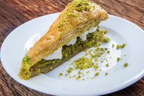 Pyszne ciasto na baklawę, warstwowe, z kremem i posypane pistacjami, na białym talerzu.