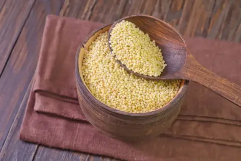 Misternie ułożona kasza jaglana w drewnianej misie, nabierana drewnianą łyżką. Odpowiedź na pytanie: czy kasza jaglana ma gluten? Jest bezglutenowa!