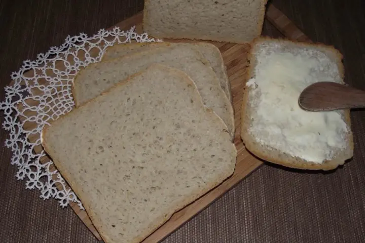 Chleb pszenno-żytni pokrojony w kromki, jedna z nich smarowana masłem. Idealny przepis na domowy wypiek.