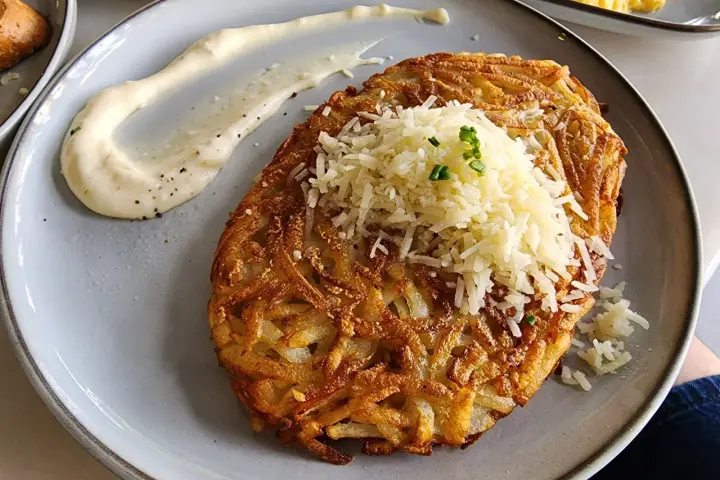 Chrupiące rosti ziemniaczane posypane startym serem i szczypiorkiem, podane z kremowym sosem.