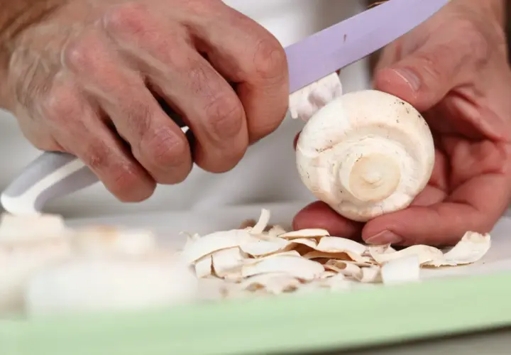 Dłonie obierają pieczarkę, tworząc stos cienkich skórek. Czy pieczarki się obiera? Tak, jeśli chcesz uzyskać delikatniejszy smak.