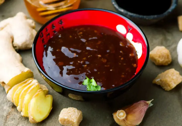 Sos teriyaki przepis: miseczka z ciemnym sosem, obok imbir, czosnek, cukier i miód. Idealny do dań azjatyckich.