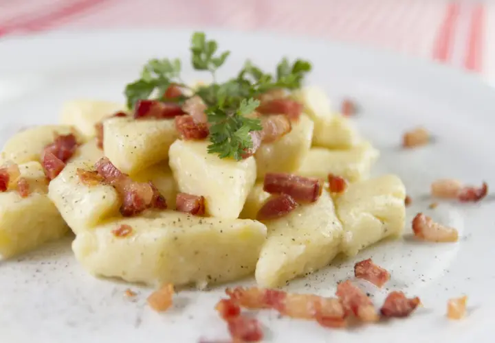 Kopytka z chrupiącym boczkiem i natką pietruszki, posypane pieprzem. Pyszne danie, które aż prosi się, by je zjeść.