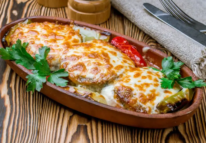 Kotlet po góralsku zapieczony z serem i warzywami w glinianym naczyniu, udekorowany natką pietruszki.