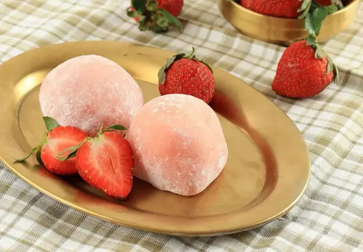 Różowe mochi z truskawkami na złotym talerzu. Idealne do wypróbowania, gdy szukasz przepisu na mochi.