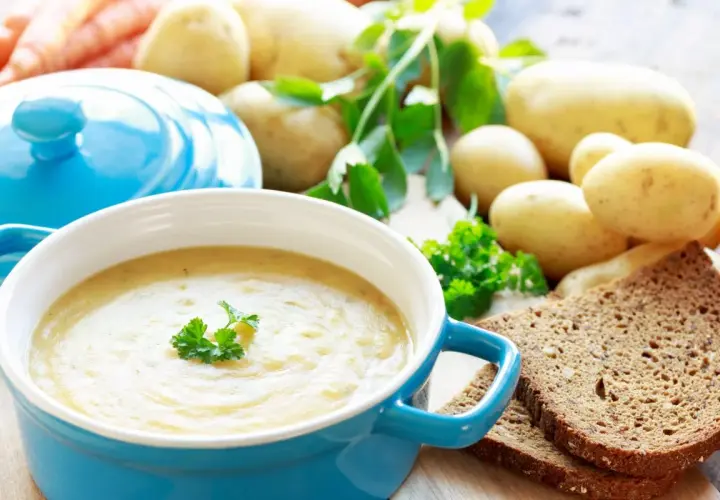 Pyszna zupa ziemniaczana przepis babci, podana w niebieskiej misce, z ziemniakami, marchewką i chlebem żytnim w tle.