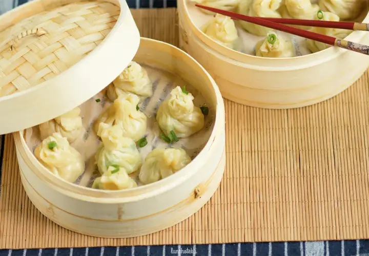 Parujące pierożki z ciasta do wontonów w bambusowych parownikach, ozdobione szczypiorkiem.