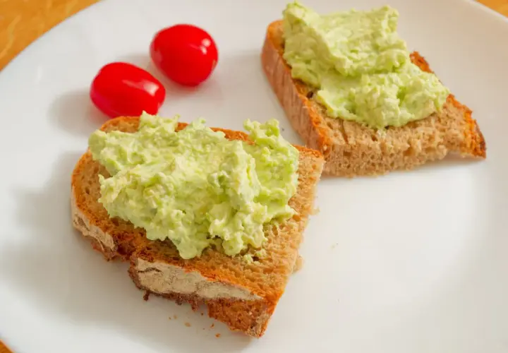 Dwa tosty z pełnoziarnistego chleba z kremową pastą z awokado i dwoma pomidorkami koktajlowymi. Idealny pomysł na szybkie śniadanie, czyli pasta z awokado przepis.