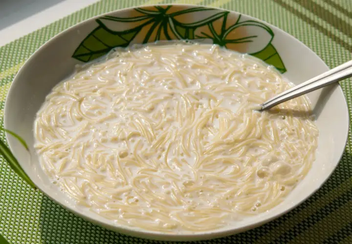 Zupa mleczna z makaronem, podana w misce z motywem kwiatowym. Widoczna łyżeczka zanurzona w kremowym daniu.