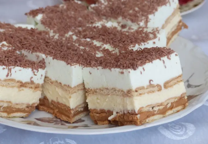 Szybkie ciasto bez pieczenia z budyniem i herbatnikami, przełożone kremem i posypane wiórkami czekoladowymi.
