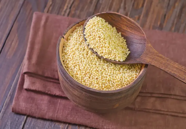 Misternie ułożona kasza jaglana w drewnianej misie, nabierana drewnianą łyżką. Odpowiedź na pytanie: czy kasza jaglana ma gluten? Jest bezglutenowa!