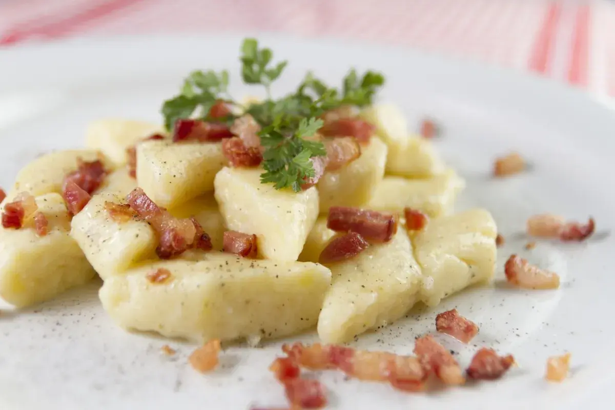Kopytka z chrupiącym boczkiem i natką pietruszki, posypane pieprzem. Pyszne danie, które aż prosi się, by je zjeść.