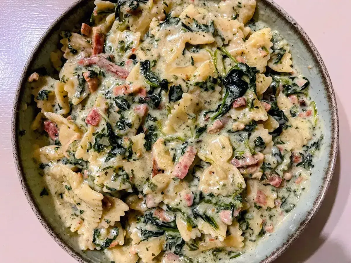 Makaron farfalle w kremowym sosie szpinakowym z kawałkami boczku. Pyszne danie, które zachwyci każdego.