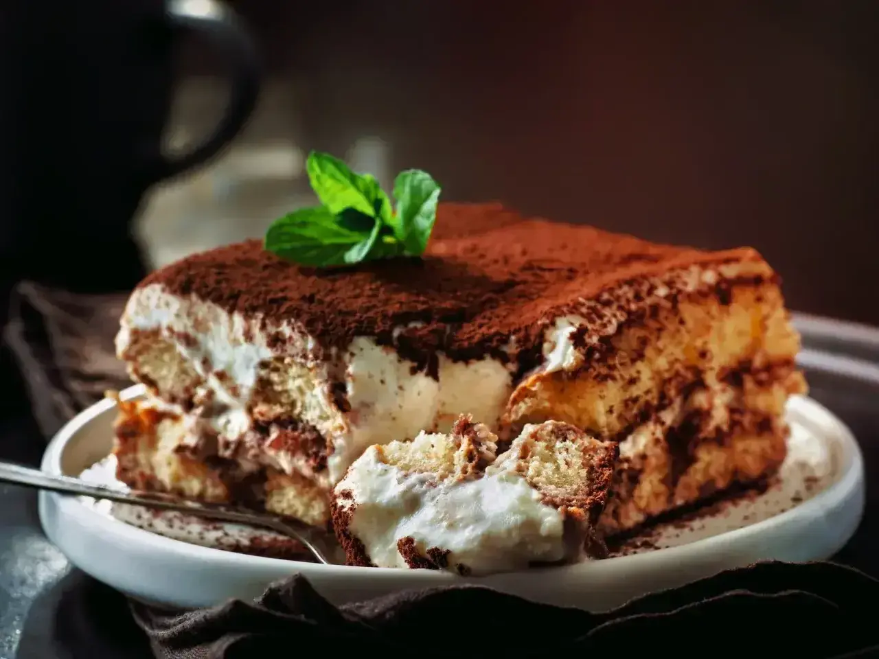 Pyszny, sprawdzony przepis na tiramisu z mascarpone. Kremowe warstwy biszkoptów i mascarpone, posypane kakao, z listkiem mięty.