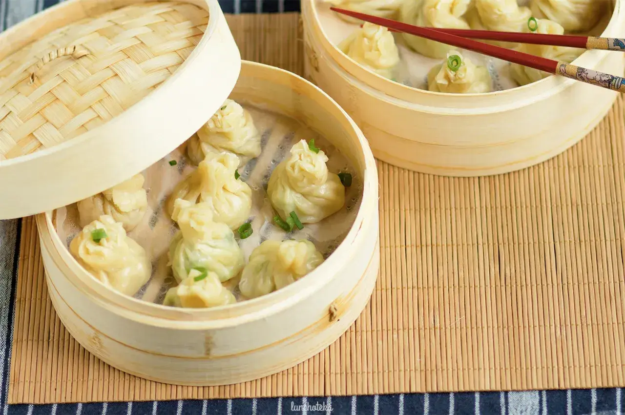 Parujące pierożki z ciasta do wontonów w bambusowych parownikach, ozdobione szczypiorkiem.