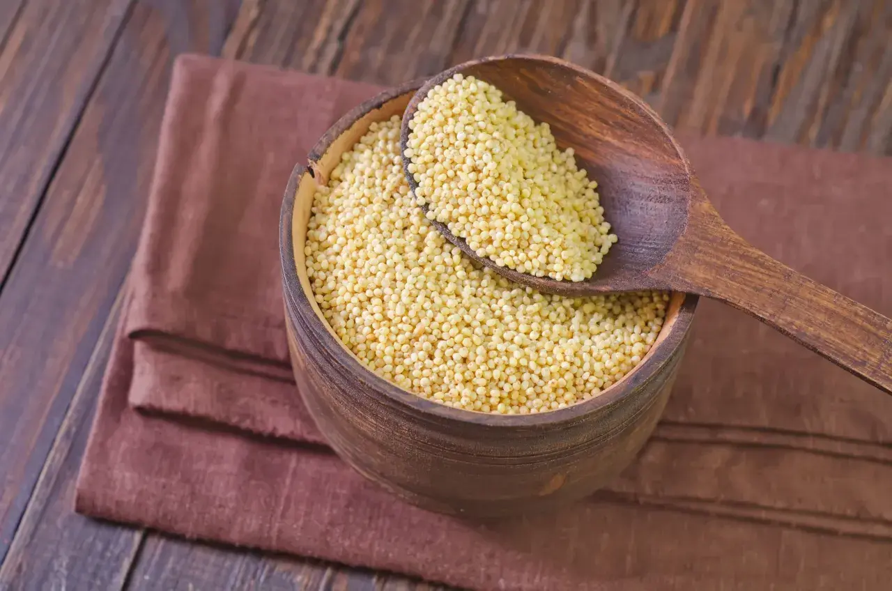 Misternie ułożona kasza jaglana w drewnianej misie, nabierana drewnianą łyżką. Odpowiedź na pytanie: czy kasza jaglana ma gluten? Jest bezglutenowa!