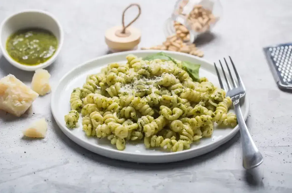 Pyszny makaron z pesto, posypany parmezanem, z dodatkiem świeżej bazylii i orzeszków piniowych.