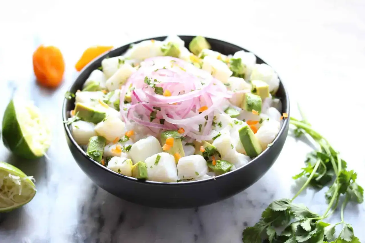 Pyszne ceviche z kawałkami ryby, awokado, czerwoną cebulą i kolendrą, podane w czarnej misce.