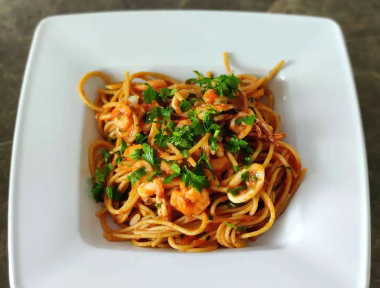 Pyszne spaghetti z krewetkami, kalmarami i małżami w sosie pomidorowym, posypane świeżą natką pietruszki. Makaron z owocami morza wygląda apetycznie.