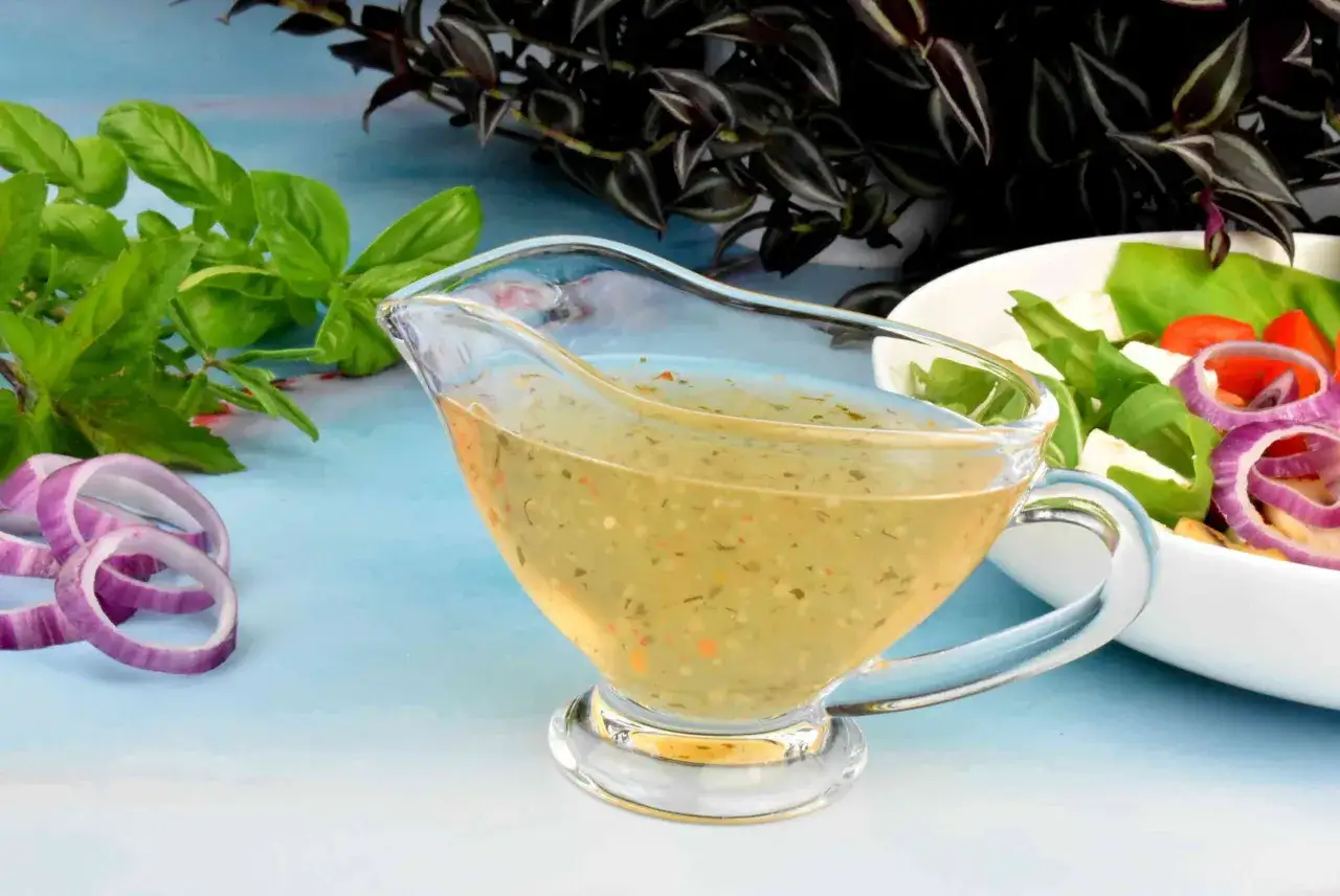 Jak zrobić sos winegret? Aromatyczny dressing w sosjerce, obok świeżej bazylii, cebuli i sałatki.