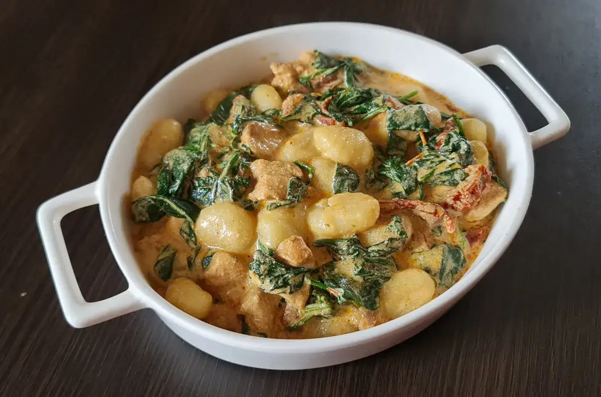 Pyszne gnocchi z kurczakiem i szpinakiem w kremowym sosie, podane w białej misie.